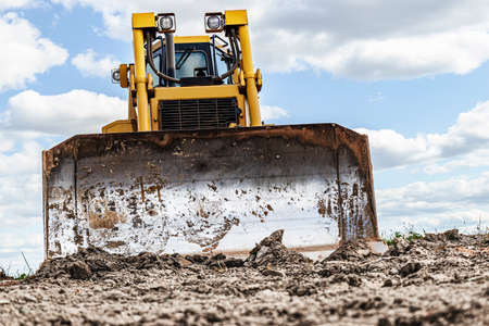 Bulldozer machine is leveling construction site. Earthmover with caterpillar is moving earth. Close-up. Construction heavy machineryの写真素材