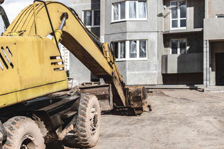 A heavy crawler excavator with a large bucket is getting ready for work in front of a panel house under construction .. Heavy construction equipment for earthworks. Quarry excavatorの写真素材