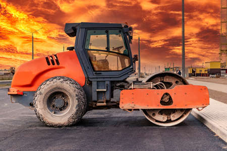 Heavy-duty vibratory roller for asphalt paving against the backdrop of a bright sunset sky. Road construction. Construction of roads and urban transport communicationsの写真素材
