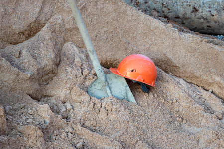 A shovel covered in concrete in a pile of sand to prepare concrete and an orange construction...