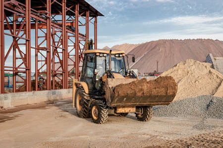 An excavator in the front bucket removes soil for backfill at the construction site. Construction...
