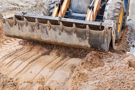 The excavator backfills the pit with the front bucket. Moves soil around the construction site. Close-up. Heavy construction equipmentの写真素材