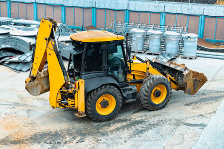 A multipurpose excavator with a front bucket transports soil to the construction site. View from...