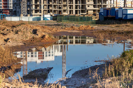 A large puddle after rain at the construction site of a large residential building. Reflection in the water of a construction site and cranes on a sunny dayの写真素材