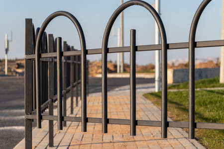 A metal fence between the roadway and the sidewalk. An empty pedestrian path with a fence. Multi-lane road with a pedestrian path next to it separated by a railingの写真素材