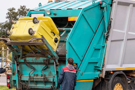 A garbage truck picks up garbage in a residential area. Workers load a container with garbage....