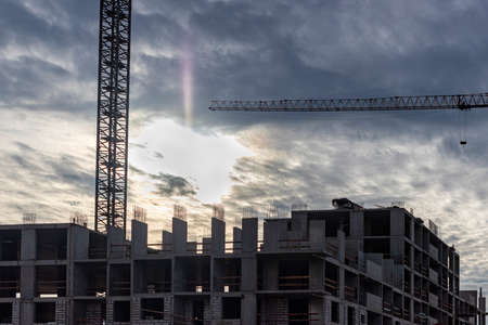 Construction of a panel frame house at sunset using a tower crane. Back light. Work at night on the construction of a residential buildingの写真素材