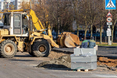 A heavy front loader transports earth in a bucket and grades the road. Road repair in the center of...