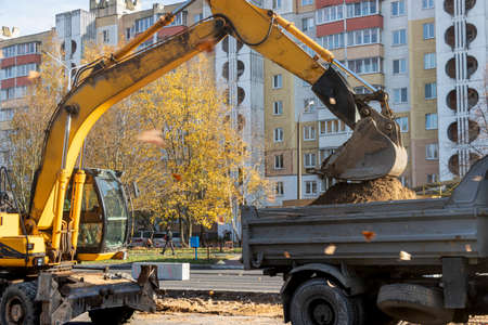 An excavator in a modern city is carrying out work during the reconstruction of the road. Repairs in the city with heavy construction equipmentの写真素材