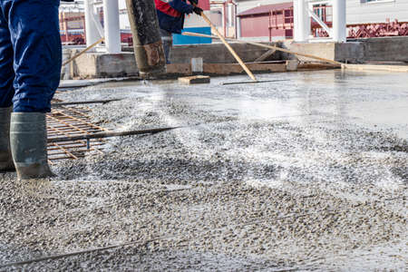 Builders workers pour concrete floor in industrial workshop. Legs in boots in concrete. Submission of concrete for pouring the floor. Monolithic concrete worksの写真素材