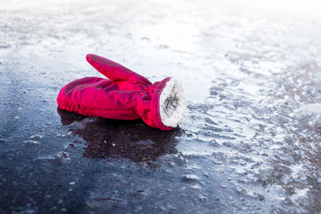 A child's mitten on a slippery road made of melted ice. Spring thaw and ice. Winter road in the city. Injury and consequences after a fall on an icy roadの写真素材