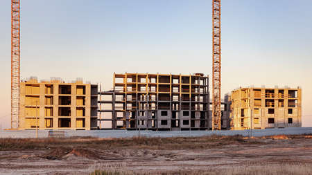 Construction of a panel frame house at sunset using a tower crane. Back light. Work at night on the construction of a residential buildingの写真素材