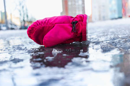 A child's mitten on a slippery road made of melted ice. Spring thaw and ice. Winter road in the city. Injury and consequences after a fall on an icy roadの写真素材