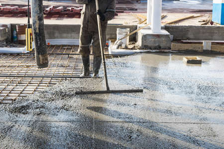 Construction worker leveling a poured concrete floor in an industrial workshop. Legs in boots in concrete. surface concreting. Monolithic reinforced concrete worksの写真素材