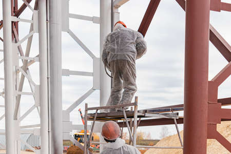 A worker in special protective clothing, works on painting and fire protection of metal structures at a height. Painting the metal at the construction siteの写真素材