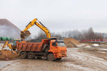 An excavator loads soil or sand into a dump truck. Pit development. Earthworks with the help of...