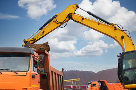 An excavator loads soil or sand into a dump truck. Pit development. Earthworks with the help of...