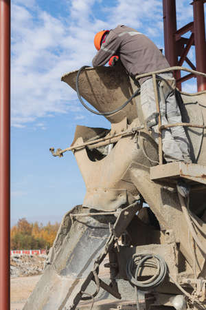 A worker on a concrete mixer truck prepares to concrete a reinforced concrete structure. Equipment...