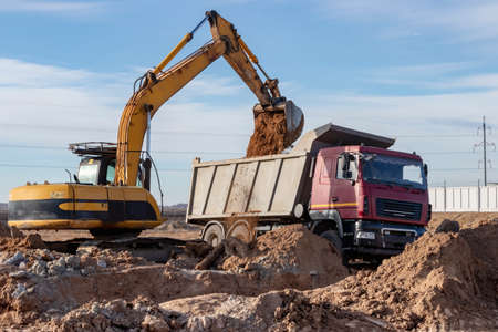 A powerful crawler excavator loads the earth into a dump truck against the blue sky. Development and...