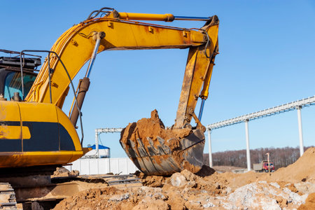 A powerful caterpillar excavator digs the ground against the blue sky. Earthworks with heavy equipment at the construction siteの写真素材