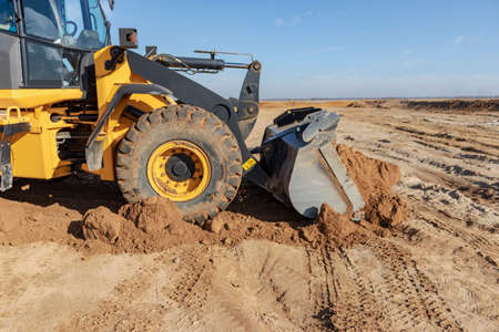 Bulldozer or loader moves the earth at the construction site against the blue sky. An earthmoving...