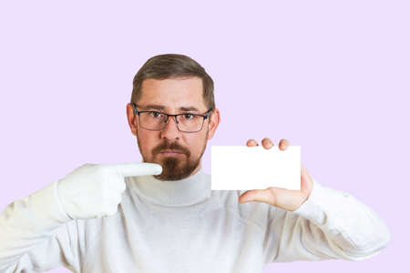 Portrait of an attractive bearded guy in glasses pointing with a finger in a white glove at a business card or ad. Isolated pastel colored background. Mocapの写真素材