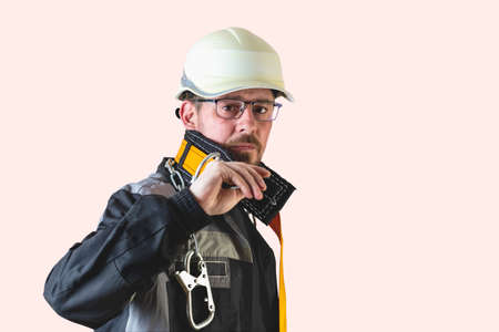Positive friendly bearded male builder in overalls and safety hardhat and goggles looking at the...