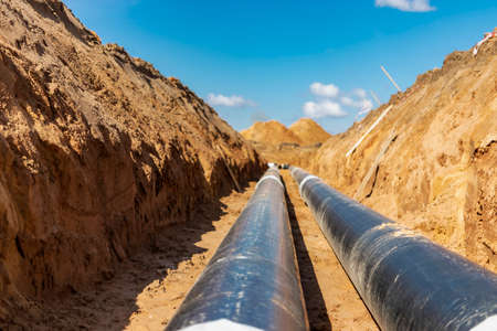 insulated pipe. Large metal pipes with a plastic sheath laid in a trench. Modern pipeline for supplying hot water and heating to a residential areaの写真素材