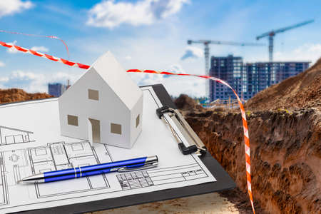 A tablet with a drawing and a mock-up of a paper house on the background of a construction site....