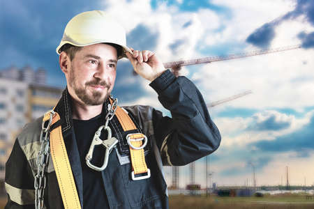 A male builder in a white hard hat against a blurred background of a construction site with a blue...