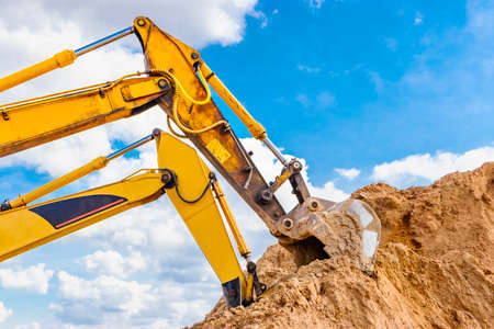 Two powerful excavators work at the same time on a construction site, sunny blue sky in the...
