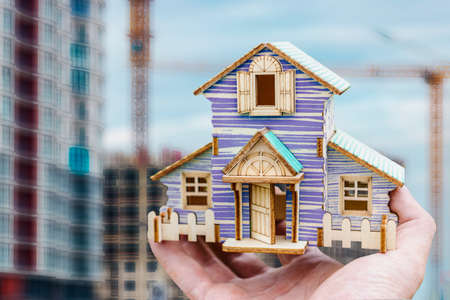 A model of a house in an outstretched hand against the background of a construction site. real...