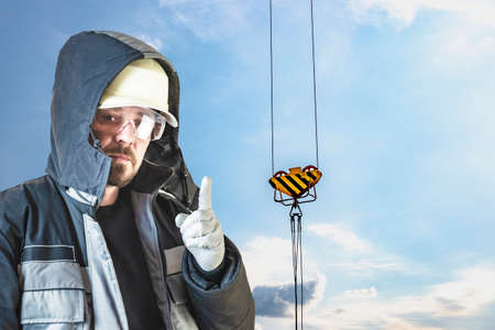 A male builder in a white hard hat against a blurred background of a construction site with a blue sky. Positive civil engineer with a beard. Safety precautions during construction workの写真素材