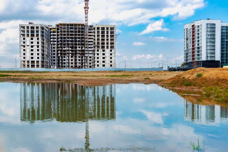 A large puddle after rain at the construction site of a large residential facility. Reflection in the water of the construction site and cranes against the background of the sunset skyの写真素材