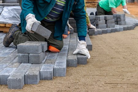 Laying gray concrete paving slabs in house courtyard driveway patio. Professional workers bricklayers are installing new tiles or slabs for driveway, sidewalk or patio on leveled sand foundation baseの写真素材