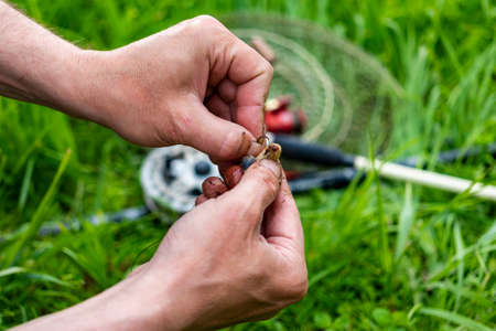 Close up Men's hands put bait on hook to fish with fishing rod. Lifestyle, recreation, leisure concept. Fisherman with wormの写真素材