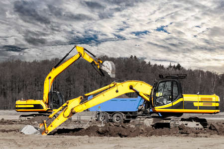 A powerful crawler excavator loads the earth into a dump truck against the blue sky. Development and...