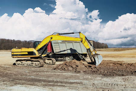 A powerful crawler excavator loads the earth into a dump truck against the blue sky. Development and...