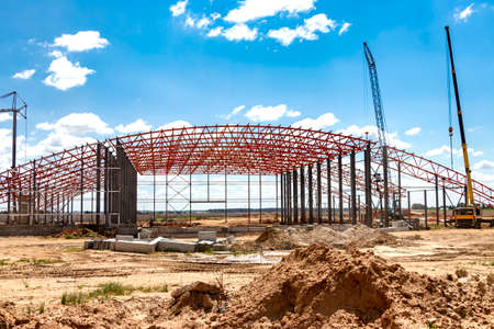 Installation of metal trusses and frame during the construction of an industrial building or factory. The work of installers during the installation of the roof. Construction of a large frame shopの写真素材