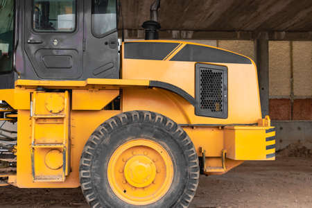 Heavy wheel loader with a bucket at a construction site. Close-up. Equipment for earthworks, transportation and loading of bulk materials - earth, sand, crushed stoneの写真素材
