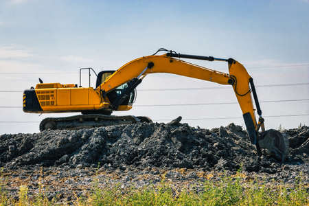 A powerful excavator digs the ground against the blue sky. Earthworks with heavy equipment at the...