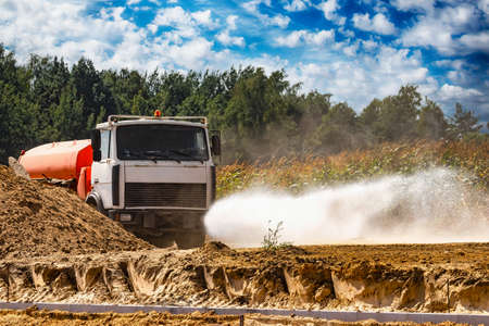 A heavy truck pours water on the road at a construction site where paving slabs will be laid. Dust removal, environmental protection. Irrigation of the road from dust and soil compaction in constructionの写真素材