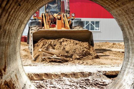 A large front loader pours sand into a pile at a construction site. Transportation of bulk...