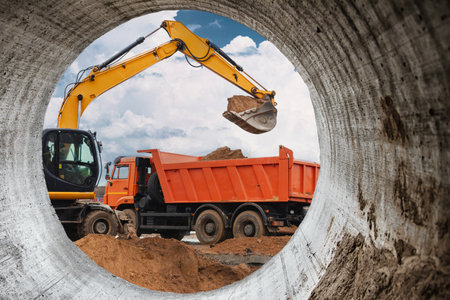 A powerful crawler excavator loads the earth into a dump truck against the blue sky. Development and removal of soil from the construction siteの写真素材