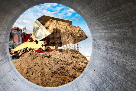 A large front loader pours sand into a pile at a construction site. Transportation of bulk...