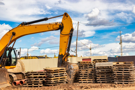 Powerful excavator at a construction site against a blue cloudy sky. Earthmoving equipment for construction. Excavator among wooden palletsの写真素材