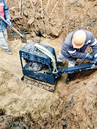Workers tamp the soil with special working tool - tamping machine or vibratory plate. foundation preparationの写真素材