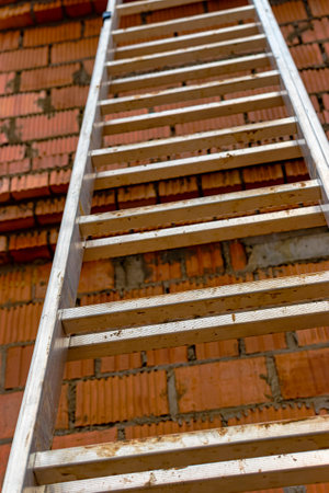 Aluminum ladder at the construction site against the background of a red brick wall. Work at height. safety engineeringの写真素材