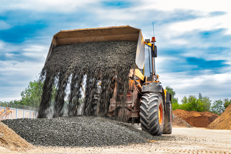 Powerful wheel loader or bulldozer on sky background. Loader pours crushed stone or gravel from the bucket. Powerful modern equipment for earthworks and bulk handlingの写真素材