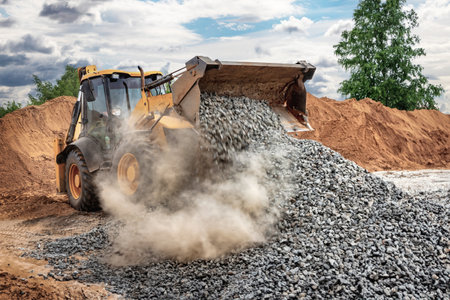 Powerful wheel loader or bulldozer on sky background. Loader pours crushed stone or gravel from the...